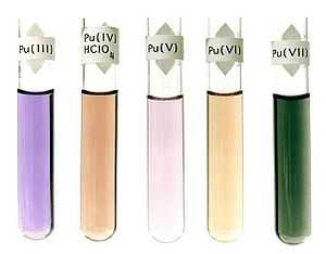 Five liuids in glass bottles: violet, label Pu(III); dark brown, label Pu(IV)HClO4; light purple, label Pu(V); light brown, label Pu(VI); dark green, label Pu(VII).