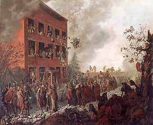 Burning three-story house, surrounded by a mob. People are throwing things out of the windows and belongings are scattered on the street.