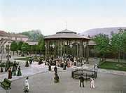 A gazebo-structure with drinking fountains at the base, in a tree-lined square.