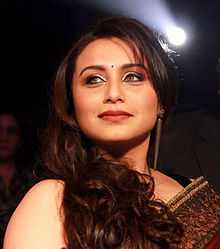 Rani Mukerji is dressed in a red saree and is smiling away from the camera