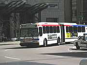 A white bus in two sections, connected by a black expansion joint, goes into a turn.