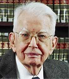 Coase looking to the camera and smiling, wearing a suit and tie