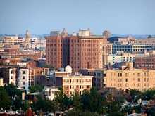 A tall red brick building in the center of a city skyline punctuated by steeples and other shorter buildings.