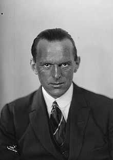 A head and upper torso portrait of Tryggve Gran, middle-aged man with receding hair and a weathered complexion, looking directly to camera and wearing a suit and tie}