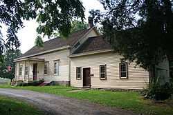 A yellow house with a road in front seen from underneath tree branches to its right