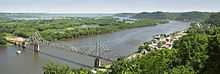 Summertime overlooking a wide and winding river.  A small town is to the right.  An old steel cantilever-truss bridge dominates the foreground.