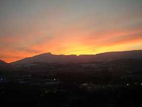 Sunset lights up the sky, silhouetting a long, notched ridge with a prominent peak toward its left-hand (southern) end.