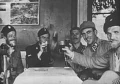 a black and white photograph of uniformed males seated arounf a table, several are holding glasses