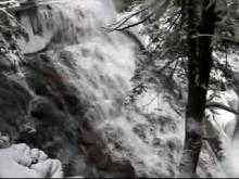  A video taken in winter from the trail starts by looking up to the head of the waterfalls and then pans slowly down and to the right to follow the falling water cascading down a stone face. The thundering water flows freely, but the surrounding rocks and trees are covered in snow and ice.