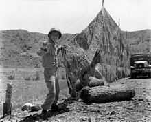 A man in military uniform constructs a net in a hilly outdoor environment