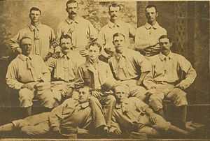 A baseball team is posing for a photograph. There are four men standing, five men sitting, and two men are laying on the ground.