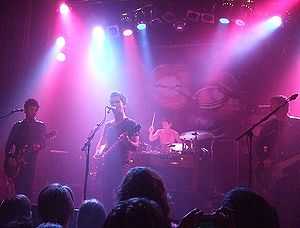 A band of four playing on a stage lit with purple lights