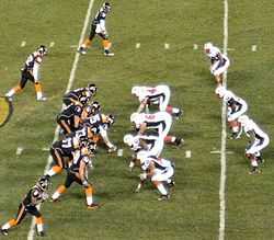 Several American football players in black and white uniforms in action at the mid-field area of the stadium.