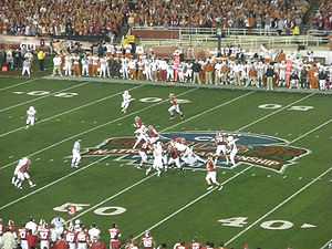 American football players in formation at the 50-yard line on a green field.