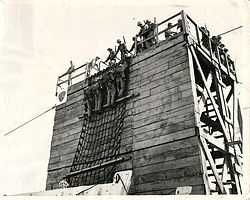 Marines climbing down cargo net into landing craft.