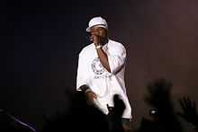 50 Cent, in white T-shirt and baseball cap, singing into a microphone