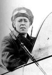 Half-portrait of man in cap and goggles seated in the open cockpit of a biplane