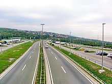 Six-lane motorway route passing through a rest area, with parking areas on both sides of the route and a filling station.