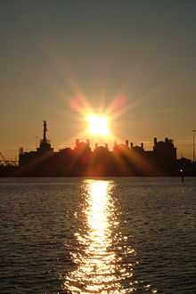 Sunset behind cluster of buildings, with water in foreground