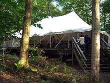 Photo of a large white tent on a wooden platform with stairs leading up to it.