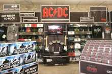 Inside a supermarket, boxes of the video game Rock Band, a display with music CDs, and a display with the AC/DC logo atop it, featuring shirts, CDs and the Rock Band instruments.