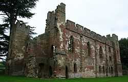 A ruined building minus a roof and with crumbling walls. Some of the walls are crenelated. The walls are build with red stones in the middle and grey stones as edging on the tops and corners.