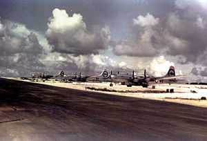 Color photo of three silver four engined World War II-era aircraft neatly lined up alongside a runway