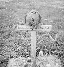 Wooden cross on grave with a steel helmet on top of cross