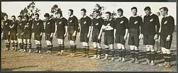 Fifteen players standing in one line while wearing rugby jerseys. The player on the far left is holding a rugby ball.