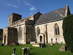 Stone building with square tower to left hand end. Foreground shows gravestones in grass area.