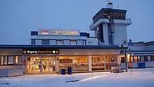 The entrance to a small airport terminal, mostly with one story, but also with a control tower to the right and a second story in the middle. On the second story is a sign with "Avinor" and "Alta lufthavn", while above the door it says "Departures"