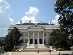 Exterior photograph of the American Red Cross Headquarters, a large, white, columned structure with red crosses on the portico peak and above the main door.