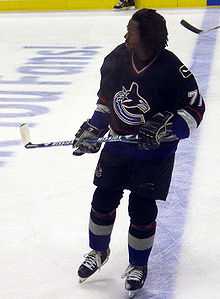 Hockey player in dark blue uniform with his helmet off. He skates on the ice, his stick held off the ground.