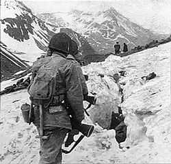 A line of soldiers hiking on the side of a snow covered mountain, viewed from behind