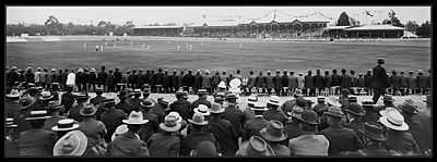 An early 20th-century cricket match, watched by a large crowd