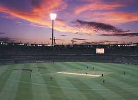 View of a cricket stadium. Batsmen in yellow outfits and fielding side in green-yellow outfits can also be seen.