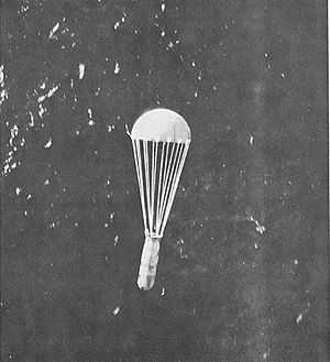 A parachute with a canister hanging below it dropping over the sea