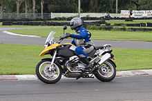  Black and yellow BMW R1200GS motorcycle, being ridden around a corner on a race track by a rider in a blue and grey suit