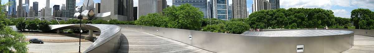 Panoramic view of a shiny metal bridge crossing a multilane road, with skyscrapers in the background.