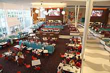 A high-angle photograph of the interior of a restaurant seating many people at booths and tables who are eating and talking under hanging light fixtures