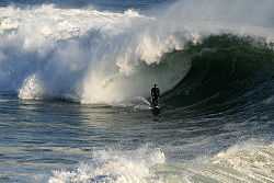 Photo of surfer at bottom of wave, attempting to let tube envelop him