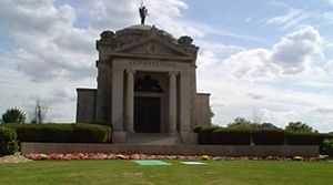 A grey stone mausoleum surrounded by a green lawn.