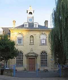 Yellow stone building with central 2 storey block with arched windows, hipped roof and clock tower