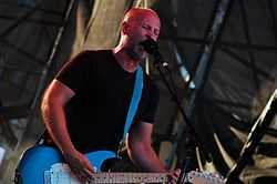 A bald man sings and plays a guitar on stage.