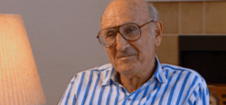 A man with grey hair, wearing a blue and white tripe shirt also wearing big red glasses