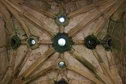 A vaulted stone ceiling. There are several circular holes in the ceiling.