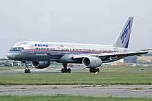 Side view of silver twin-engine jet taxiing on runway, with deployed flaps and "757" markings on tail.