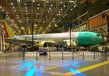 Airplane assembly hall, featuring an unpainted metallic twin-jet aircraft, a presentation podium, and arranged audience chairs.