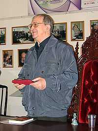 upper body of man with glasses in shirt and jacket holding an object in front with both hands