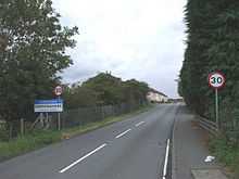 A photograph facing west along Bothkennar Road with a sign showing the entrance to the village of Carronshore.